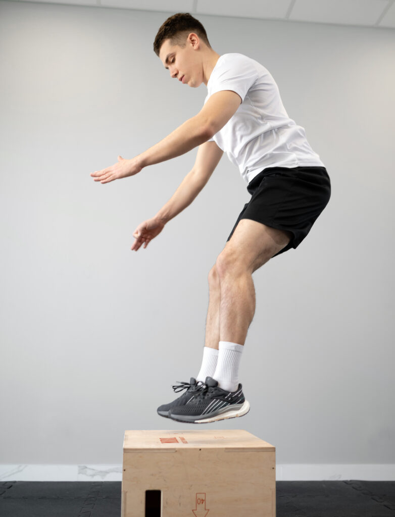 Mężczyzna wykonuje wyskok na skrzynię w ramach intensywnego treningu plyometrycznego poprawiającego siłę eksplozywną.